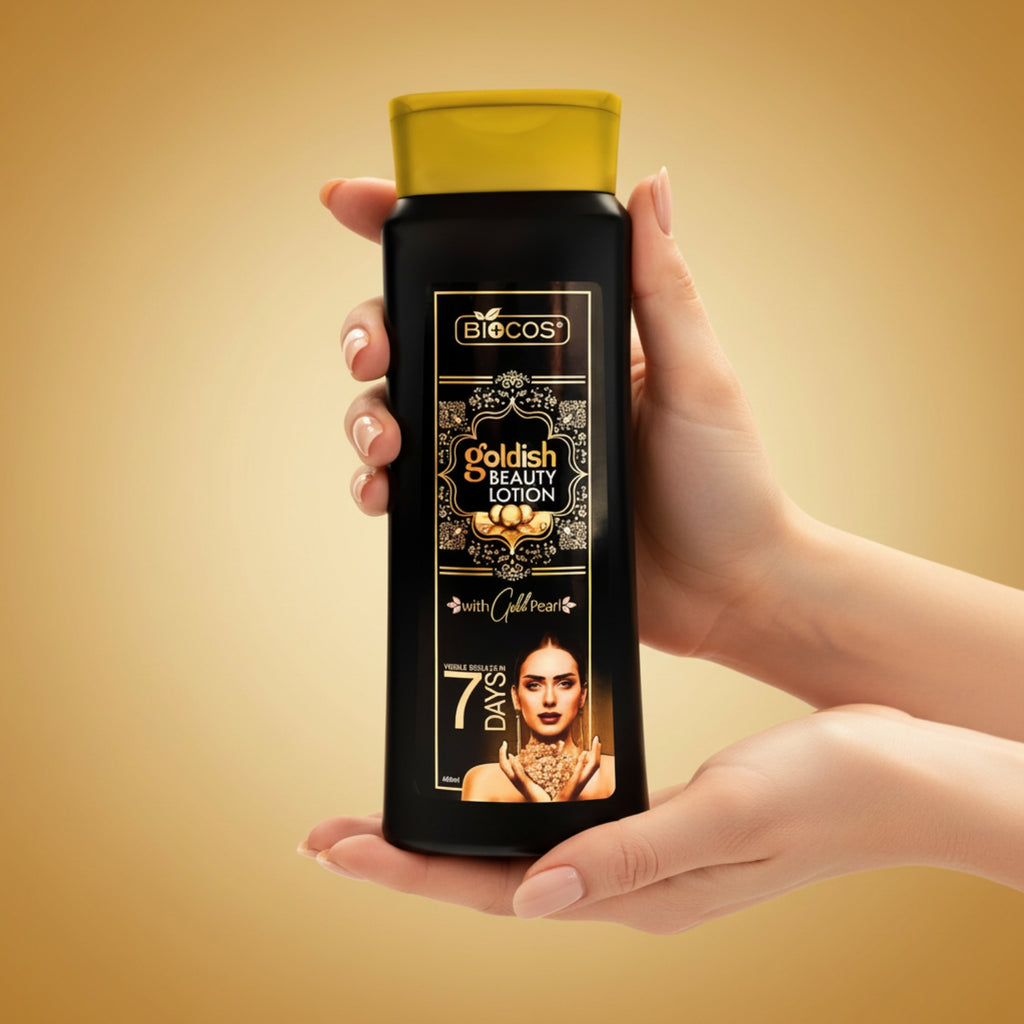 A person's hands holding a bottle of Biocos Goldish Beauty Lotion against a warm golden-brown gradient background.