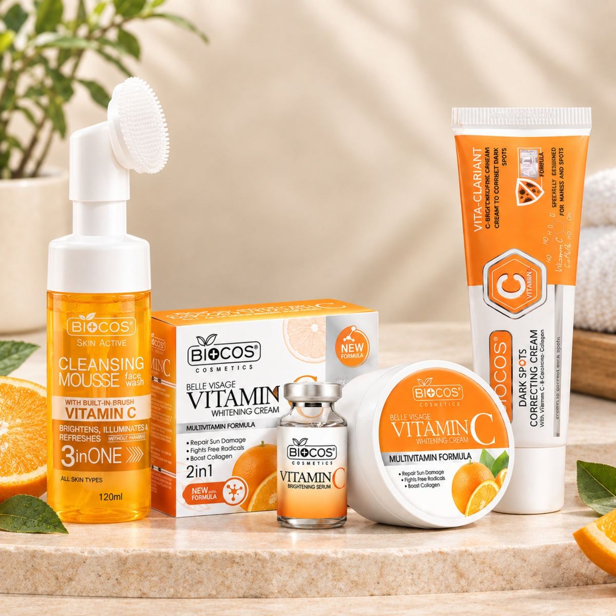 A skincare set from BioCos Cosmetics arranged on a stone surface with citrus slices and a soft neutral background. The set includes a foaming cleanser with a built-in brush, a Vitamin C brightening serum, a multi-vitamin formula in a small glass vial, a Vitamin C correcting cream tube, a Vitamin C cream jar, and a Vitamin C box.
